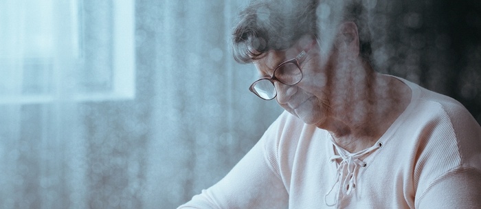 Elderly woman sitting at a table looking down.