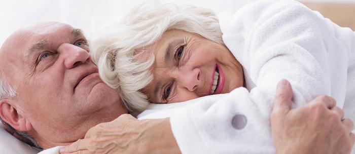 Elderly couple lying down holding each other.